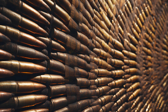 Rifle ammunition gold colored brass rounds arranged in neat rows on wall creating repetitive metallic pattern with detailed bullet tips and cartridge cases. Cartridges lined up in uniform featuring.