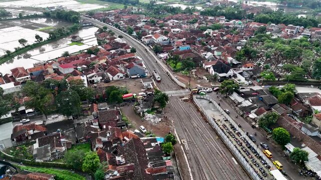 Aerial view of Cicalengka railway tracks surrounded by dense residential housing and lush green rice fields in Bandung, West Java, Indonesia.