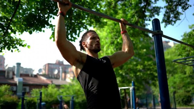 Athletic man doing pull ups on horizontal bar outdoors, athletic male training in outdoor gym park, calisthenics workout for physical fitness and body building