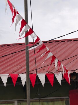 Red and white triangular bunting flags hanging outdoors against a red corrugated metal roof, traditionally used for Indonesian Independence Day celebrations.