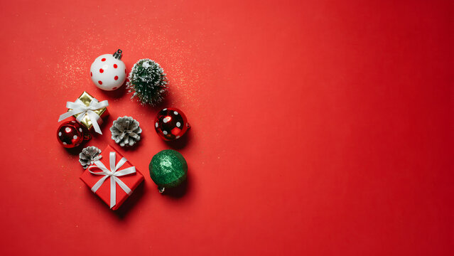 Christmas decorations including gift boxes, ornaments, and a small pine tree arranged on a vibrant red background with glitter accents