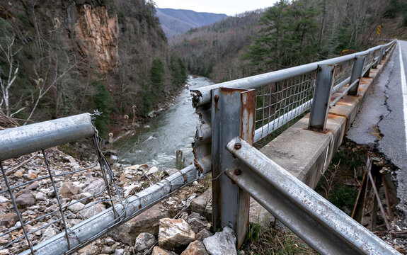 Bent steel bridge guardrail above a river gorge with a torn gap and twisted posts