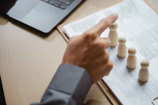 Human resources and interview selection are suggested by two people pointing toward wooden figures on paperwork beside a laptop; human resources planning and resume review frame an employment choice.