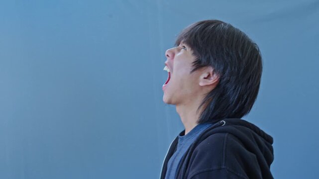 Young asian man rapidly alternates between screaming upward and covering ears in distress symbolizing bipolar mania