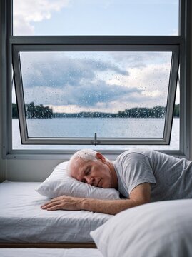 Senior man napping on a houseboat bunk by a rainy window