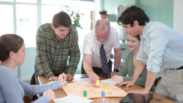 Happy group of undergraduates engaging in tabletop game with a professor during practical training 