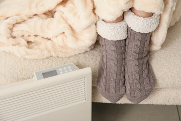 Energy efficiency and home heating, person wearing warm socks and blanket near electric heater for winter comfort and cost saving during cold weather © Pixel-Shot