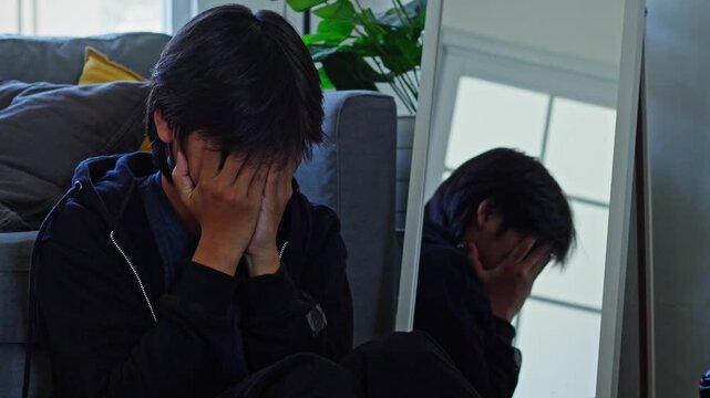Young man sits on floor covering face with hands in deep despair reflecting bipolar depression