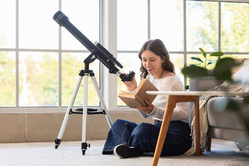 Fototapeta premium Astronomy hobby and lifelong learning, young woman reading a book while using a telescope at home for science education and personal development