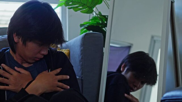 Young man sits on floor near mirror hugging himself tightly in fear and cold isolation showing bipolar distress