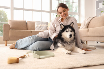 Pet care and companionship, happy woman relaxing with her husky dog at home after cleaning the floor with a brush and dustpan in a bright living room © Pixel-Shot