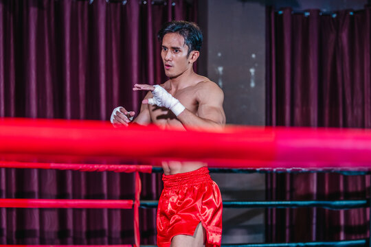 Asian boxer in red shorts shadowboxing behind ring ropes during training before fight
