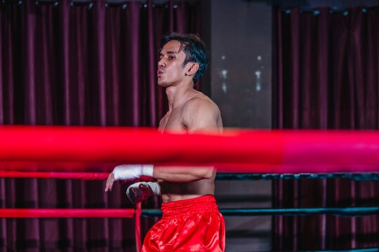Asian boxer in red shorts shadowboxing behind ring ropes during training before fight