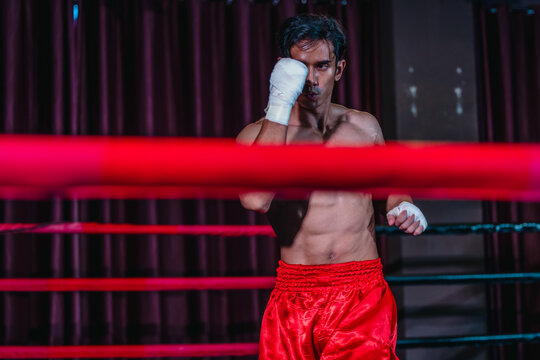 Asian boxer in red shorts shadowboxing behind ring ropes during training before fight
