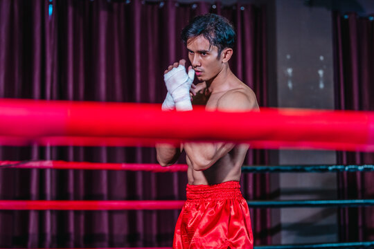 Asian boxer in red shorts shadowboxing behind ring ropes during training before fight