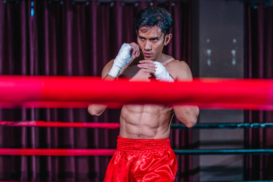 Asian boxer in red shorts shadowboxing behind ring ropes during training before fight