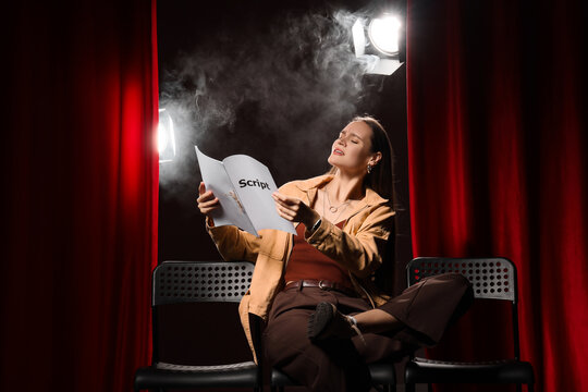Audition stress and performance anxiety, young actress practicing lines from a script on stage with dramatic spotlight and smoke in a theater setting