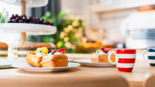 Freshly baked waffle dessert and cafe breakfast concept, crispy waffles topped with whipped cream and berries on plate beside striped coffee cup on kitchen table, symbolizing gourmet brunch.