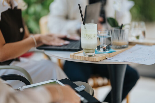 Colleagues having a business meeting in a cafe with laptops and beverages on the table. A casual work session shows people collaborating over drinks, notes, and devices at a small round table.