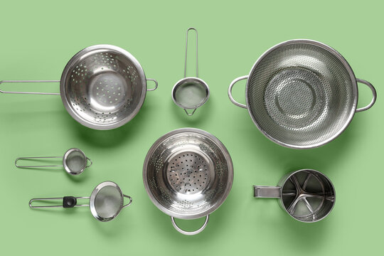 Healthy cooking and food preparation, collection of stainless steel kitchen strainers and colanders on a green background for culinary concepts
