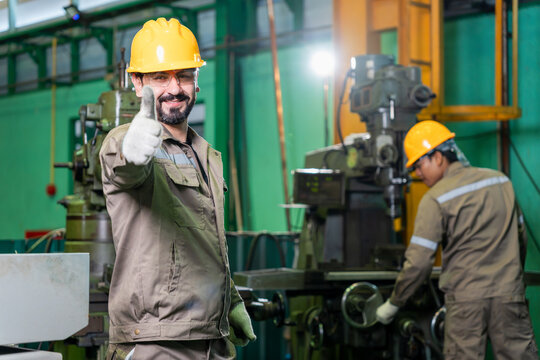 Happy technician standing in heavy machinery plant with thumbs up sign, smiling factory worker showing thumbs up gesture in manufacturing workshop