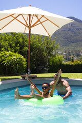 Naklejka premium African American father and son playing on neon-green ring in home pool wearing sunglasses