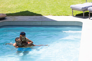 Naklejka premium African American family playing in backyard pool, father carrying child with blue goggles