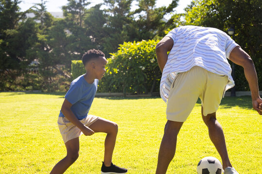 African American mature and youth males playing soccer on lawn, with ball, youth in sneakers