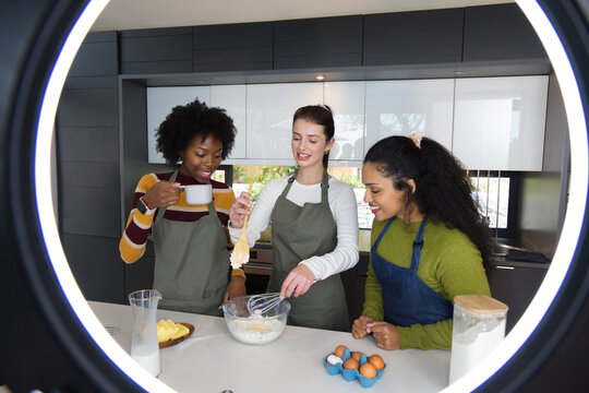 Diverse female friends wearing aprons mixing batter with whisk at kitchen island