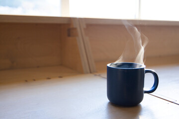 Dark blue ceramic mug is steaming on light wood countertop by window, soft sunlight, copy space © WavebreakMediaMicro