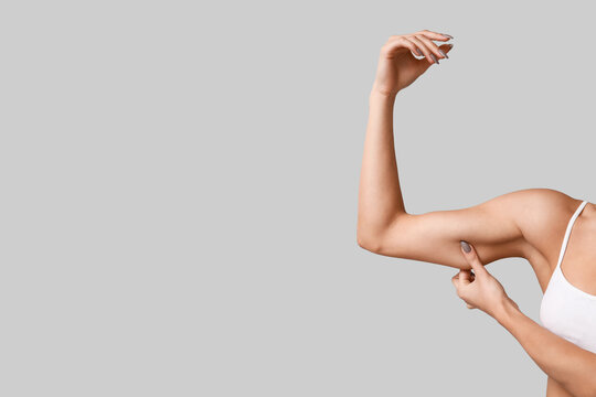 Body positivity and self acceptance, woman checking arm skin elasticity and muscle tone for skincare or fitness progress on a neutral gray background