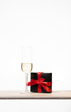 Luxury gift box with a silk bow and flute of champagne on wooden shelf . Abstract Design for e-commerce, Black Friday, seasonal sales and festive promotional offers.