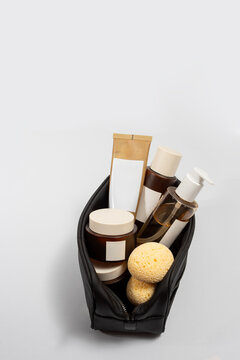 Minimalist black travel pouch filled with amber glass jars and white tubes. Ideal for a clean skincare routine on the go. Beauty essentials for organized modern travelers.