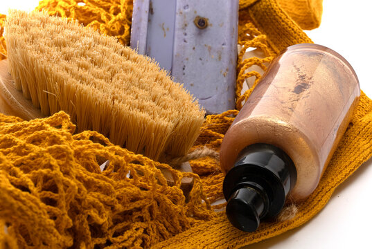A vibrant, close-up shot of eco-conscious bath essentials including a natural bristle dry brush, lavender soap, and shimmering body oil nestled in an ochre-colored mesh net bag. Perfect for travel.