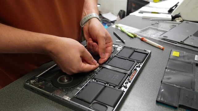 Technician disassembling and repairing an open laptop by removing internal components on an electronics workbench in a professional repair workshop