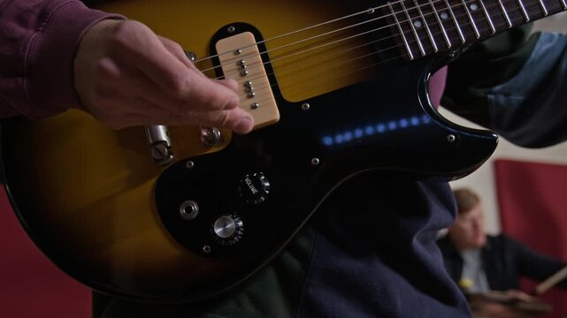 Close-up shot of unknown musician adjusting volume knobs and strumming electric guitar strings with pick. Ideal for music education campaigns, band rehearsal footage, and instrument advertisements