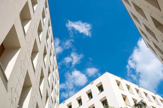 Upward view between modern apartment buildings at Aspern Seestadt Vienna Austria with geometric white facades framing blue sky and clouds