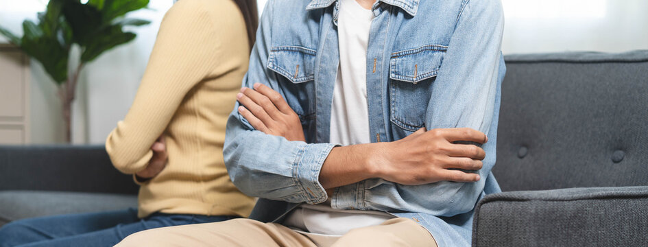 Family problem concept. Tension in relationship between married couple, husband and wife staying sitting separate after quarrel in the living room.