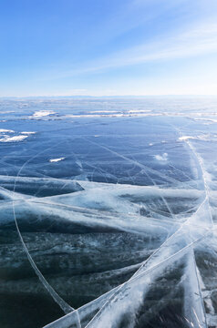 Scenic winter landscape of the frozen Lake Baikal. View of the blue clear ice surface, crisscrossed with white cracks, and the lake vast expanse on cold, sunny February day. Outdoor winter recreation