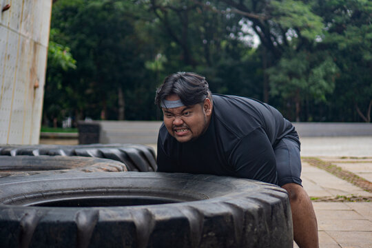 Man sitting on a tire obstacle with head down, resting after exercise