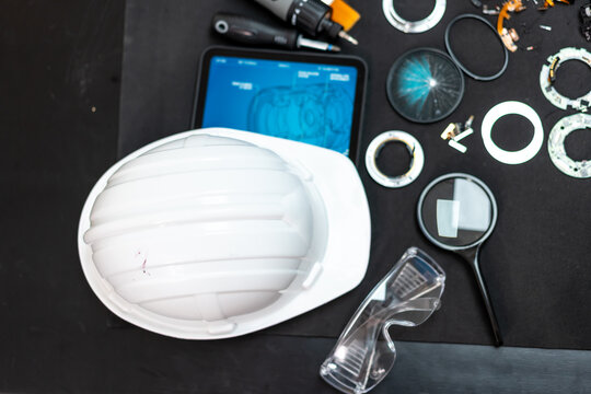 White hard hat, safety glasses, tablet and hand tools arranged on a dark workbench for industrial maintenance and inspection.