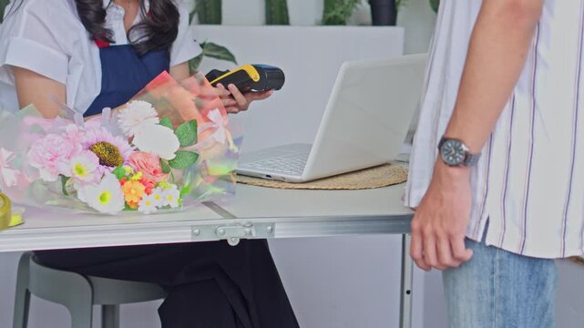 Customer pays with card via EDCT terminal while picking up floral bouquet at flower shop desk