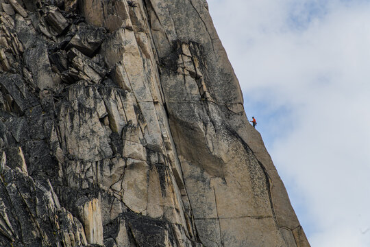 A tiny rock climber scales a massive vertical granite cliff face