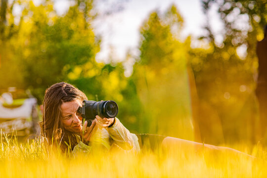 Female photographer takes a photo lying in tall grass at sunset