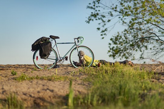 Cyclist resting on a grassy hill next to bicycle