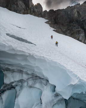 Mountaineers Ascending Snowy Slope Below Rock Wall in BC