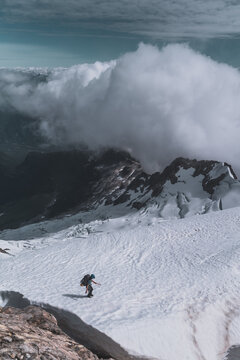 Solo Climber Descending Snowy Mountain Slope Under Large Cloud