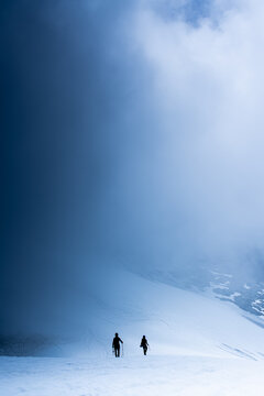Two Silhouettes of Mountaineers Walking on Snowy Mountain Ridge
