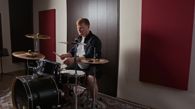 Caucasian young adult man playing acoustic drums and explaining technique in studio. Perfect for music tutorials and online masterclasses