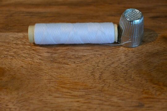 White sewing thread and metal thimble on wooden table